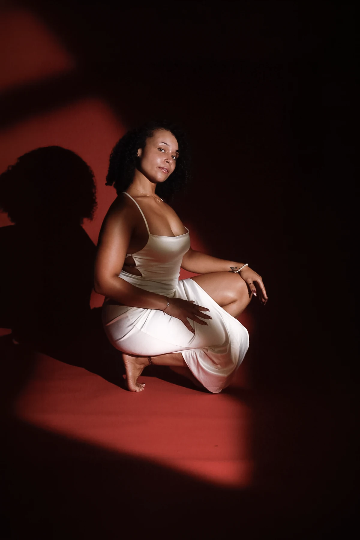 A seated studio portrait framed by graphic shadows across a deep crimson background.