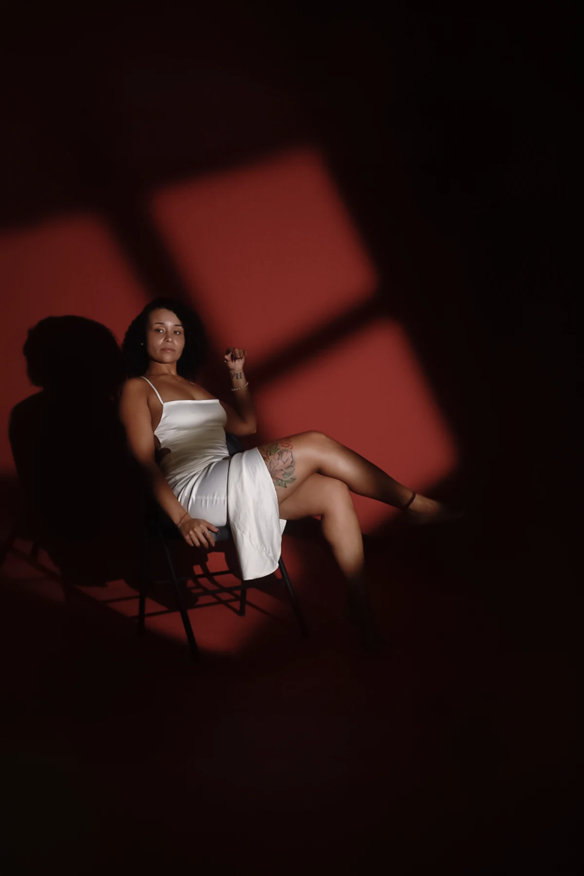 A wide, moody studio portrait with a red backdrop, a chair, and dramatic rectangular light patterns.